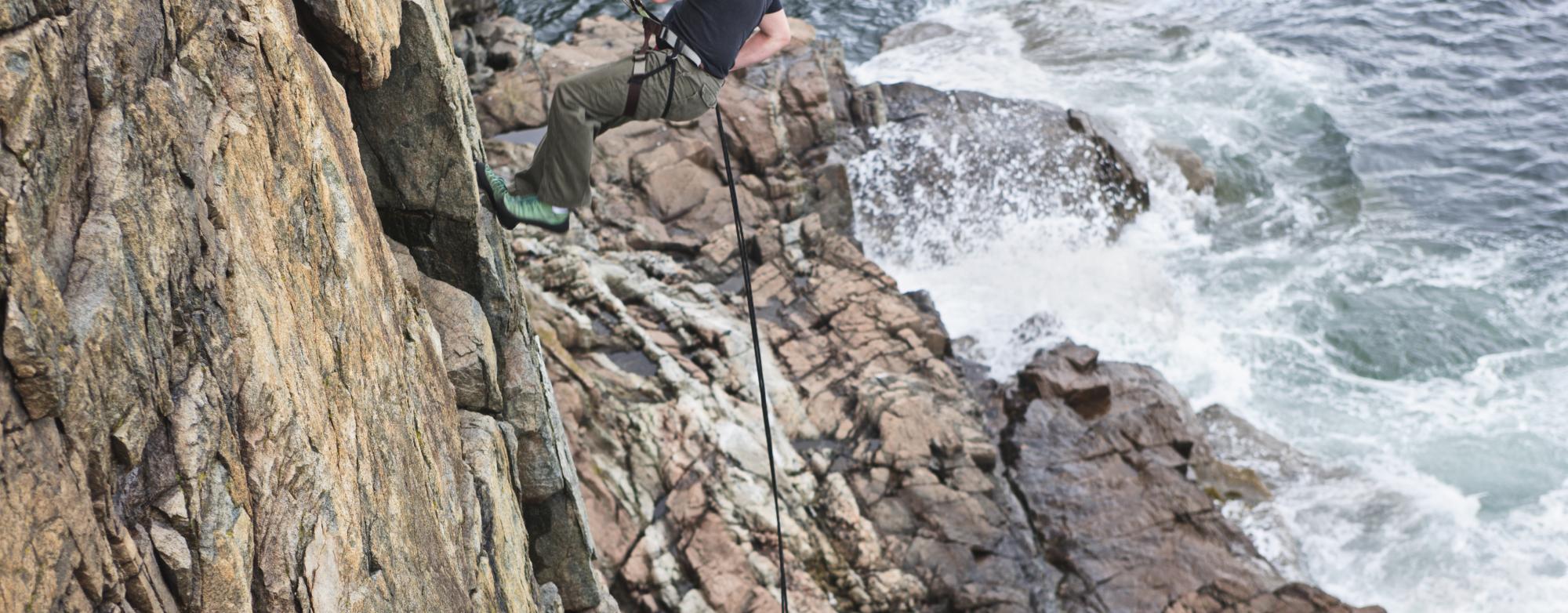 Person abseiling down the limestone cliffs of the Burren National Park with water visible below