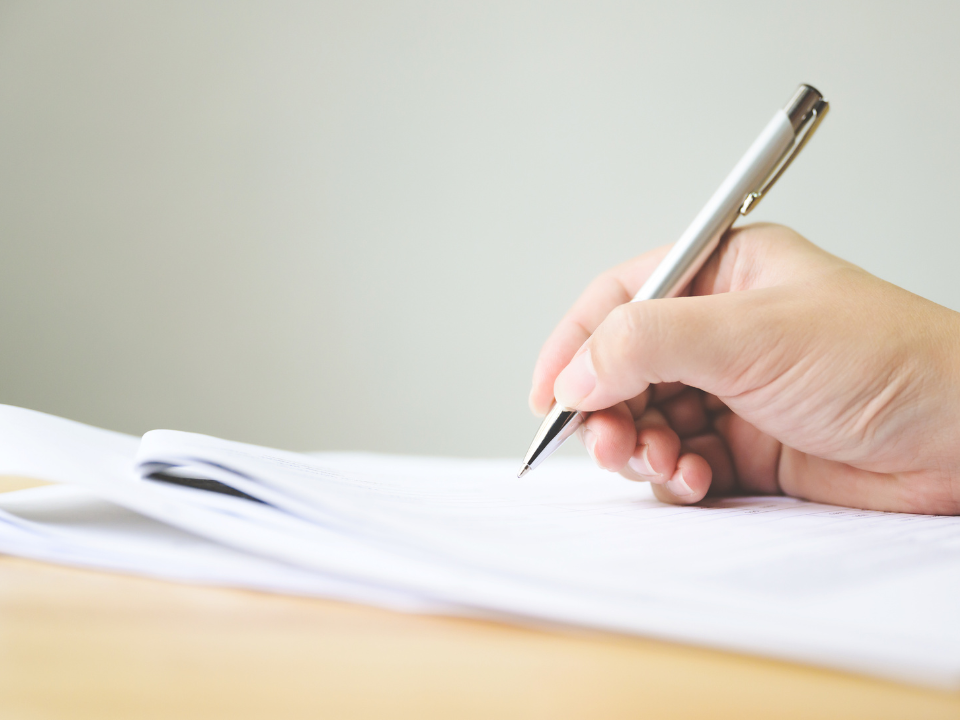 Close-up of a hand holding a pen and signing a form.