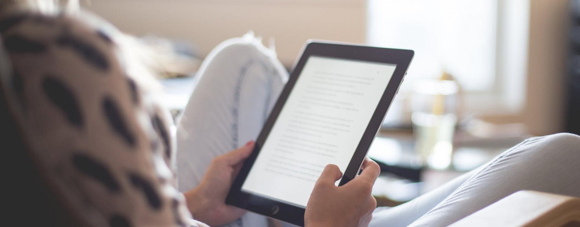 A person holding a tablet with a lit screen facing them.