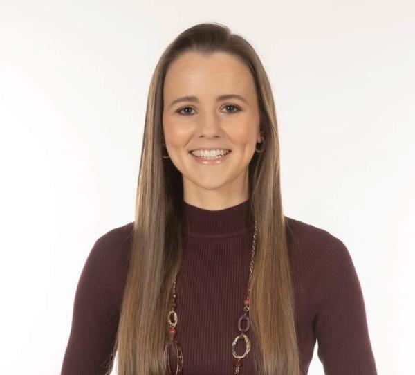 Person with long hair wearing a polo jumper, standing against a white background