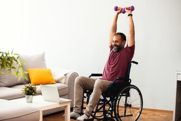 Person in a wheelchair lifting a dumbbell in a living room