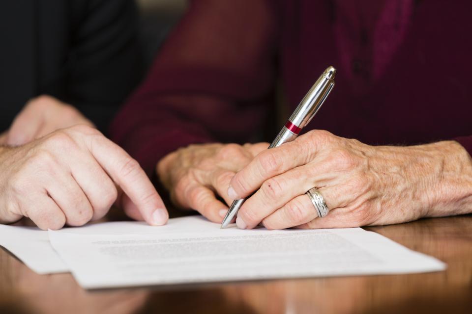 One person is writing on a piece of paper with a pen, while another person is pointing to the content on the paper