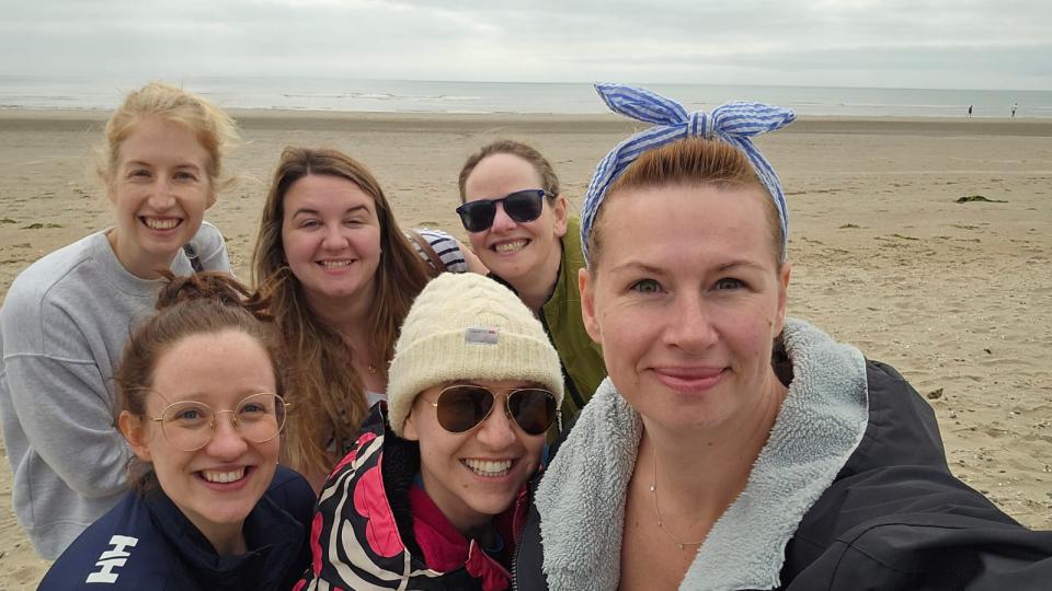 Six happy people standing on the beach after a sea swim, smiling against the backdrop of the sea, sand, and sky.