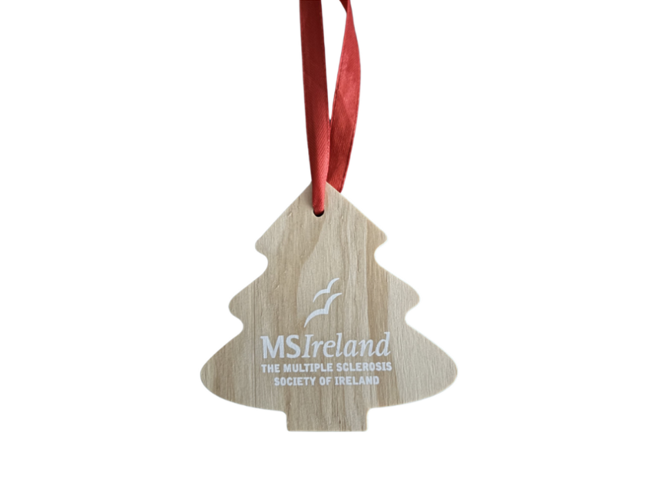 White background with a wooden Christmas tree ornament featuring MS Ireland branding and a red hanging ribbon