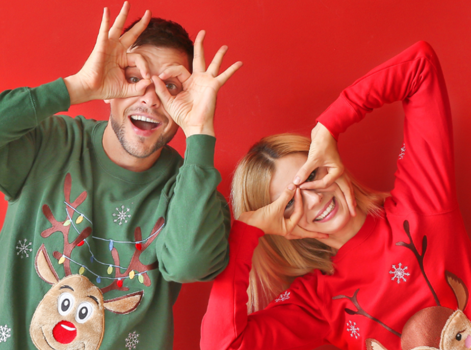 Red background, two individuals wearing festive jumpers in green and red