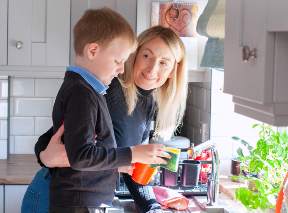 Naomi and her son standing together at the kitchen sink, with Naomi’s arm lovingly around her son, set against a cozy kitchen background.