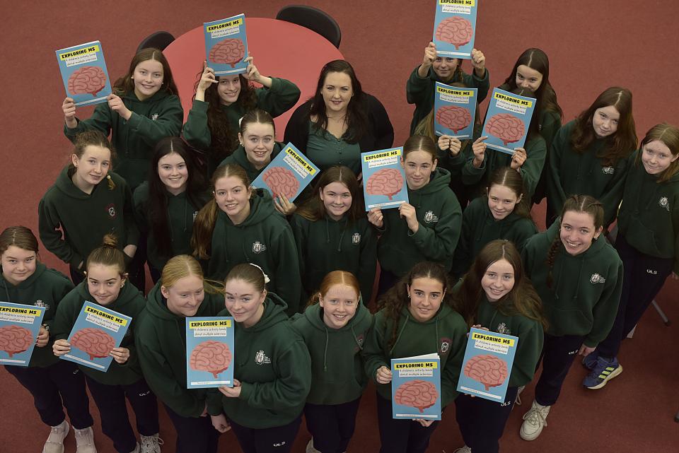 A top-down view of young students in uniform holding copies of the new Exploring MS publication, smiling and gathered together