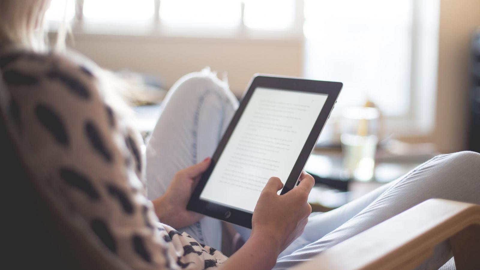 A person holding a tablet with a lit screen facing them.