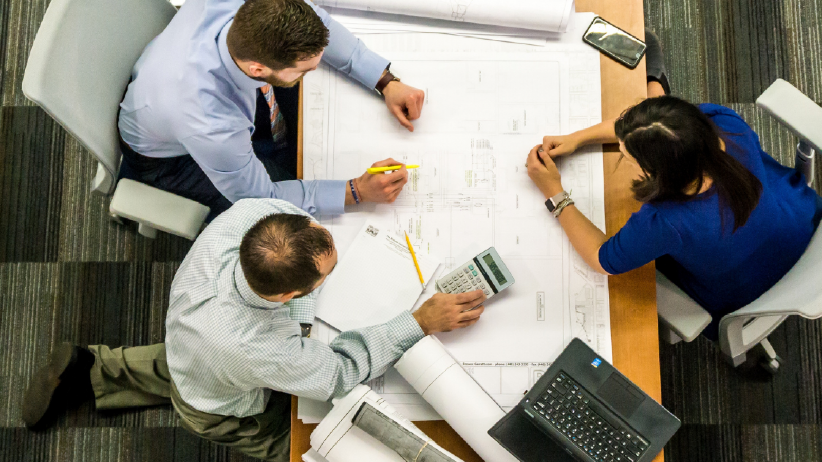 An overhead view of three individuals working together at a desk in an office setting.